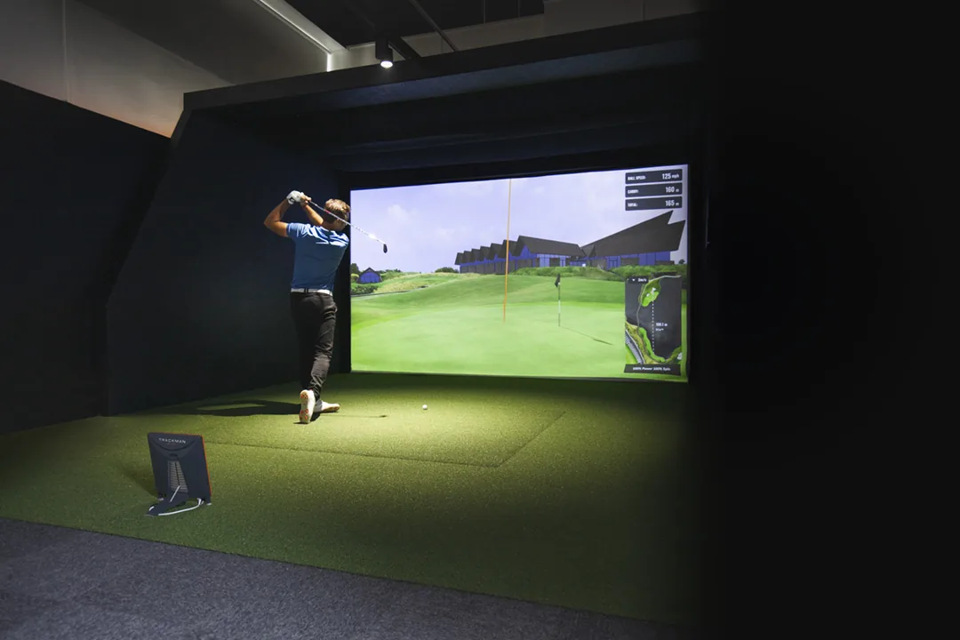 Golfer taking a lesson in a Trackman simulator bay with live shot data on screen